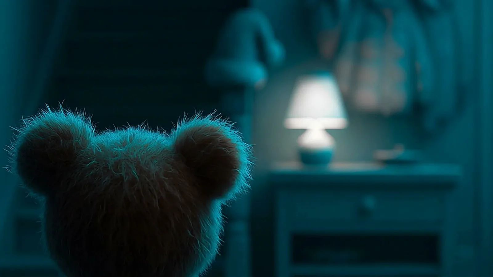 The teddy bear looks into a room lit in deep blue.