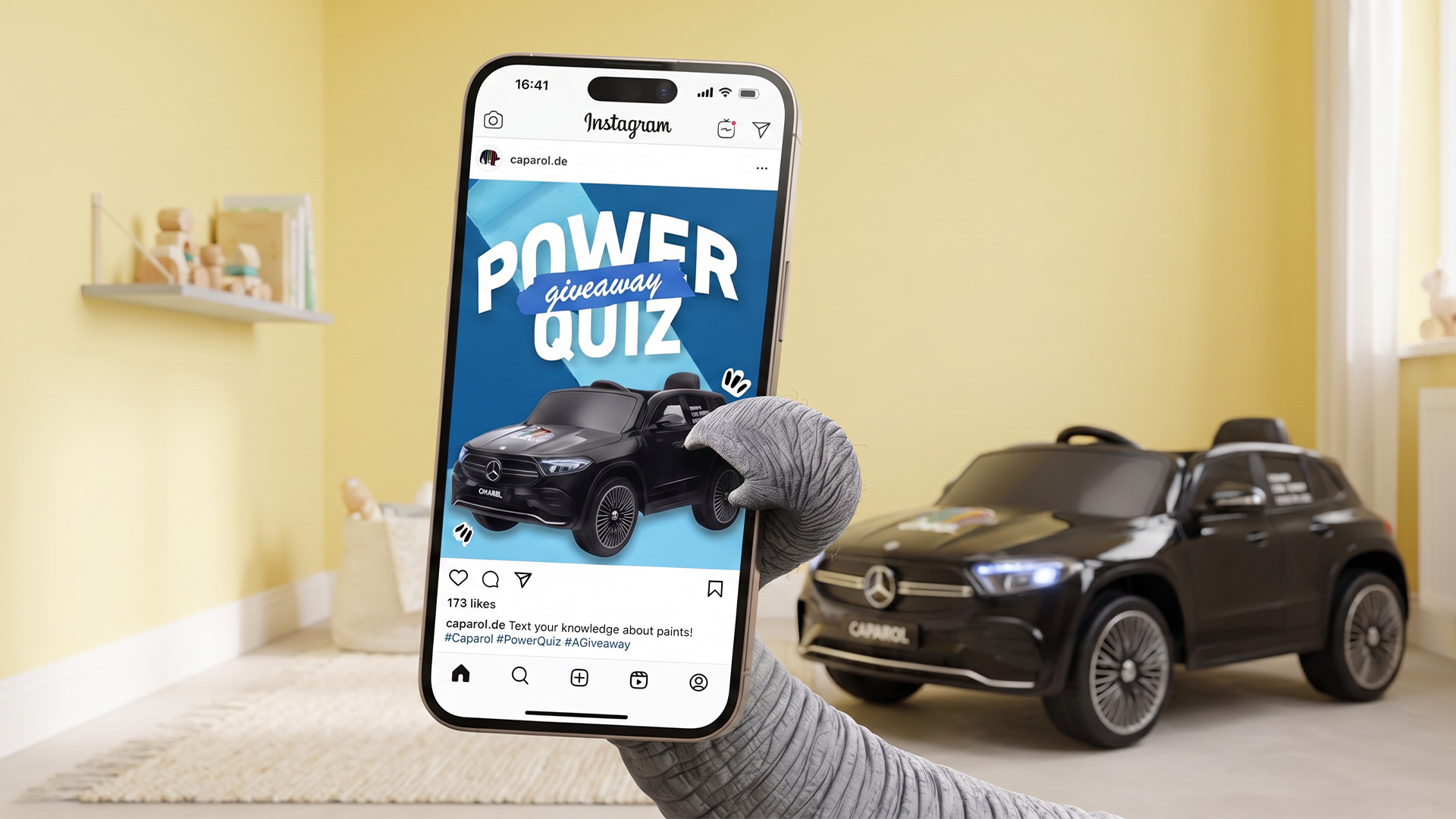 Caparol Power Quiz on a smartphone beside a black children’s ride-on car