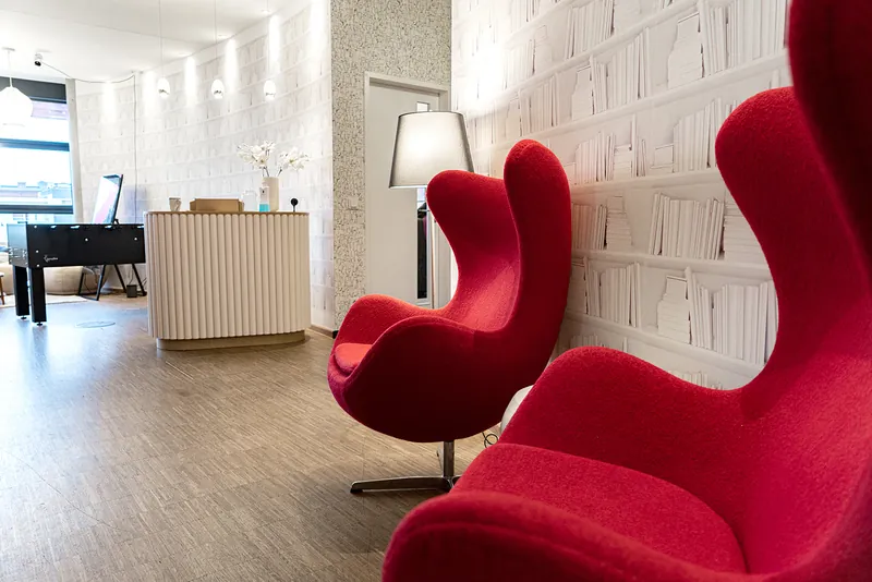 Reception area at the Hamburg office with red armchairs and bookshelf-pattern wallpaper